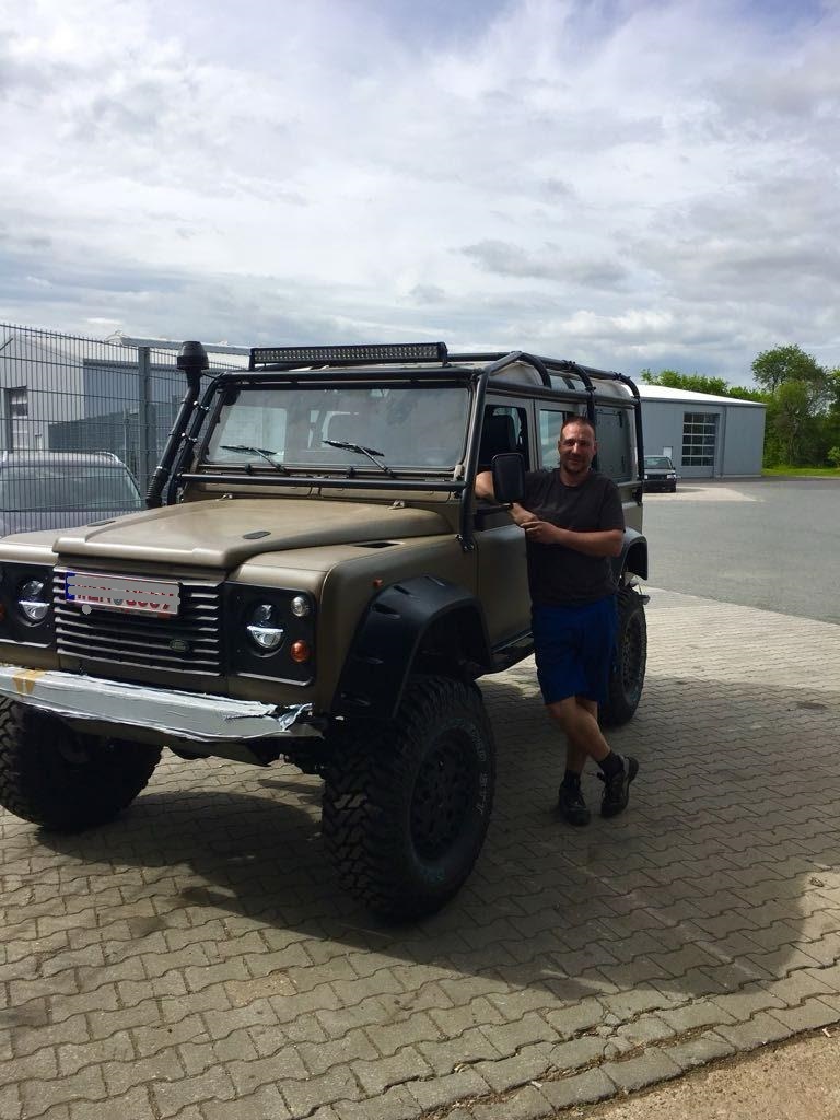 Links ein Rover auf unserem Firmengelände, an dem rechts unser Mechaniker lehnt und in die Kamera lacht.