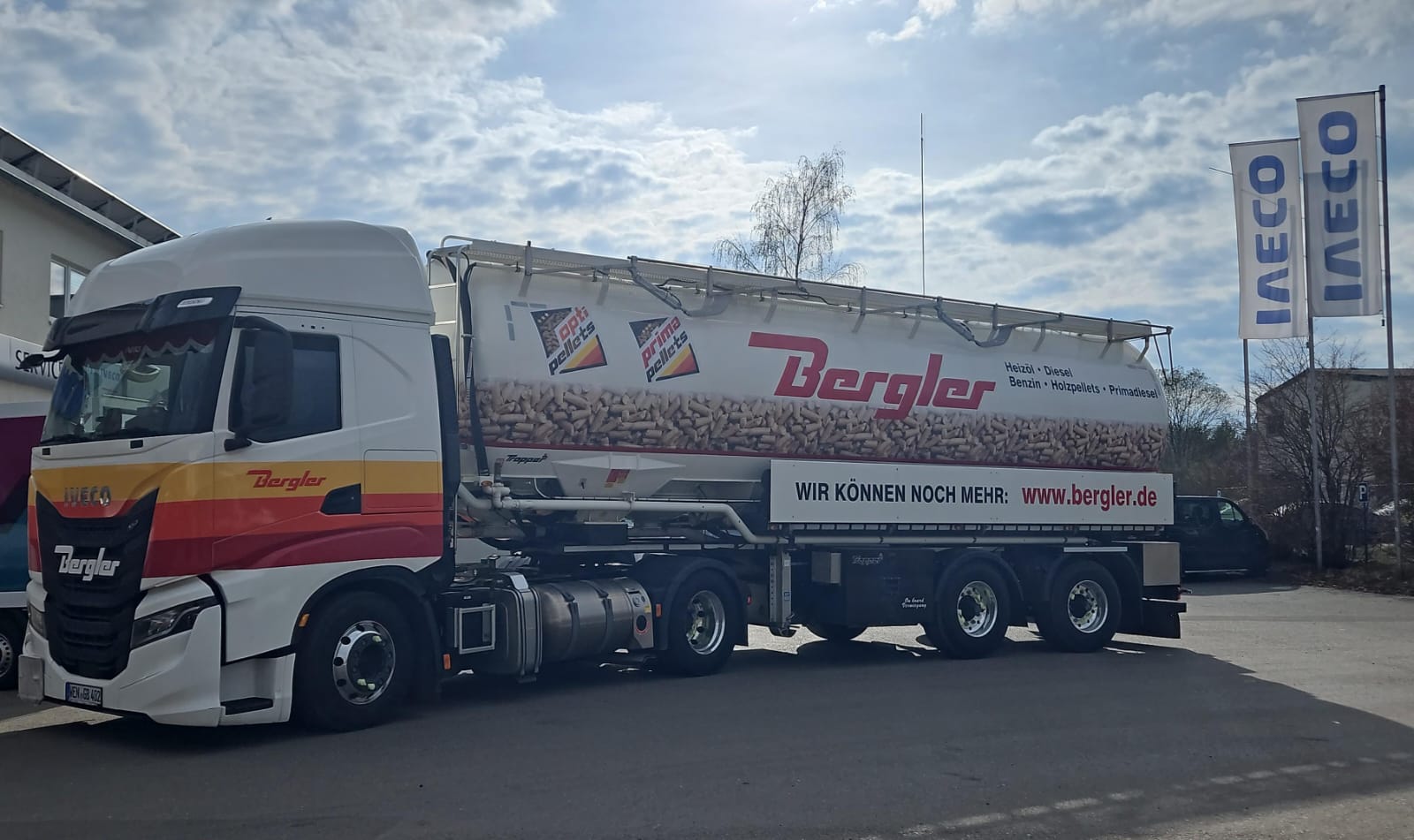 Ein weißer LKW parkt auf dem Gelände der Firma Bergler, bereit Pellets auszuliefern. Beklebt mit dem roten Bergler Logo und in schwarzer Schrift den Standorten Weiden, Marktredwitz und Amberg. Unten ist eine Folie, bedruckt mit losen Pellets, aufgebracht. im Hintergrund blauer Himmel.