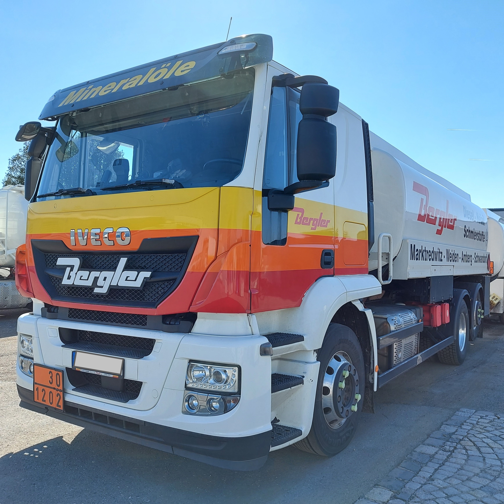 Frontansicht eines LKW mit den Bergler Farben gelb, orange und rot. Über der Fahrerkabine steht in gelber Schrift "Mineralöle".
