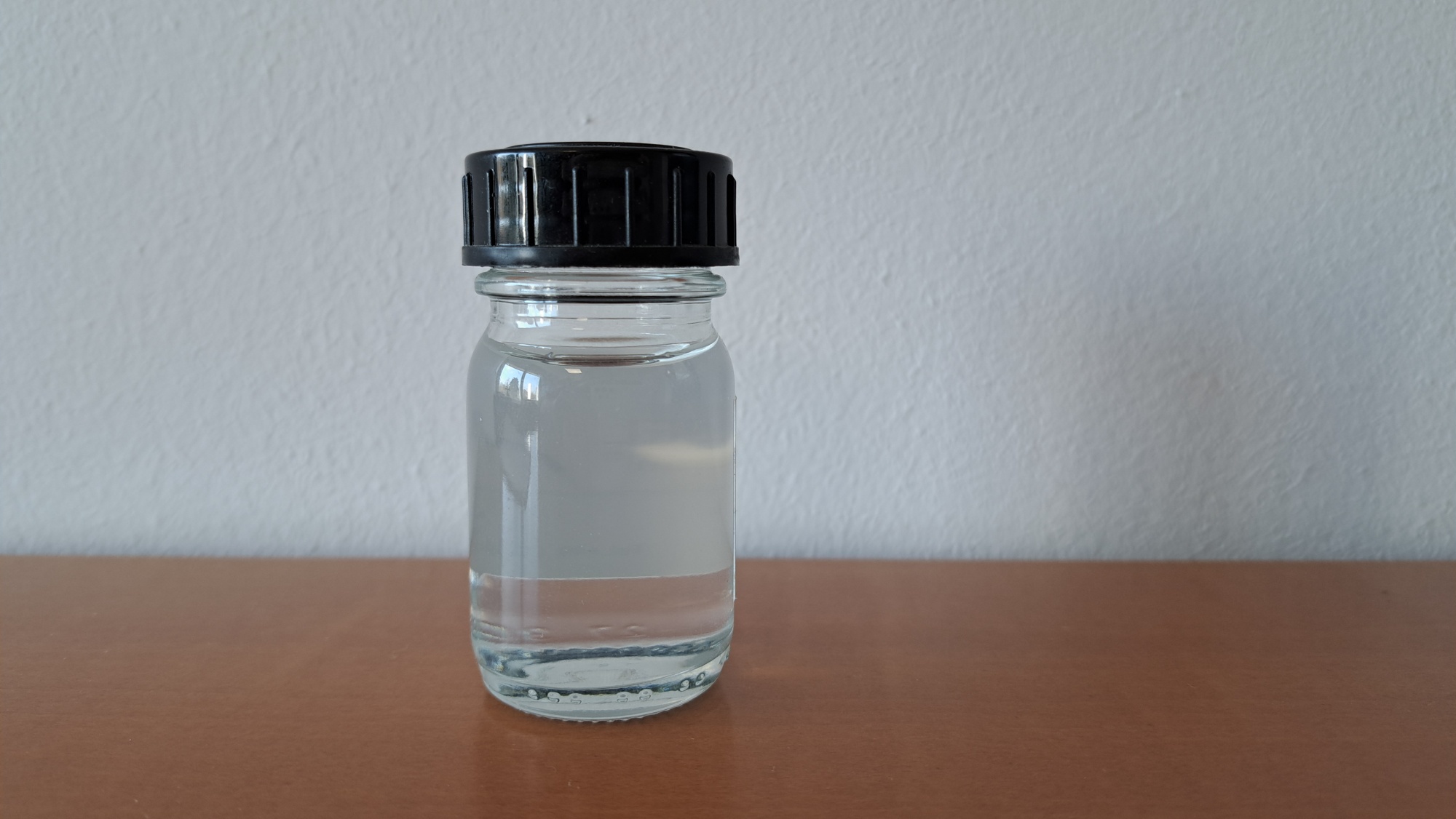 Zugeschraubte Flasche steht auf einem Tisch. Zu sehen ist flüssiges, durchsichtiges HVO. 