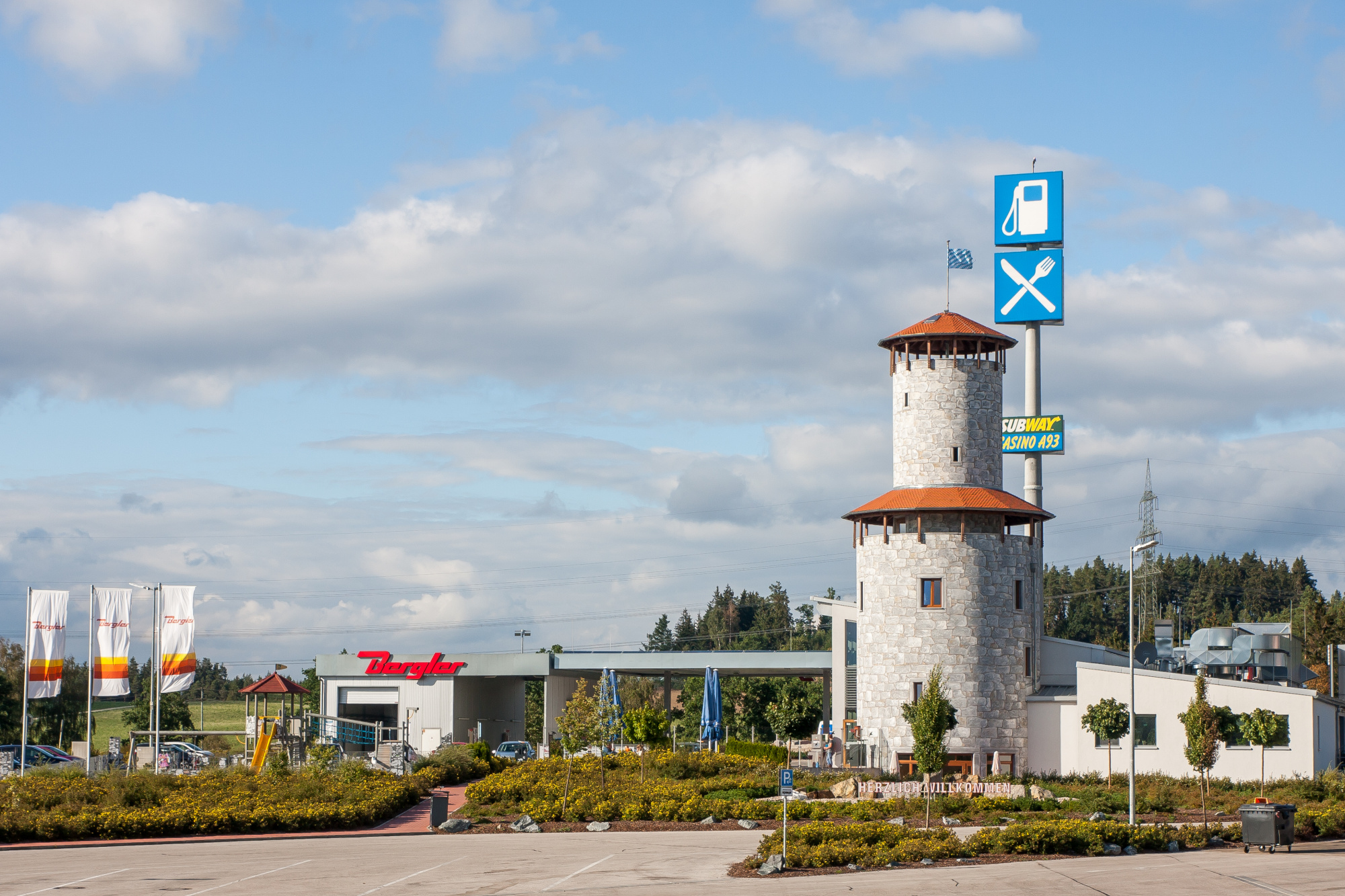 Zu sehen der Bergler Autohof, links drei wehende Fahnen mit Bergler Logo, mittig Waschplatz und Tankplatz und rechts der markante Ritterturm mit Restaurant