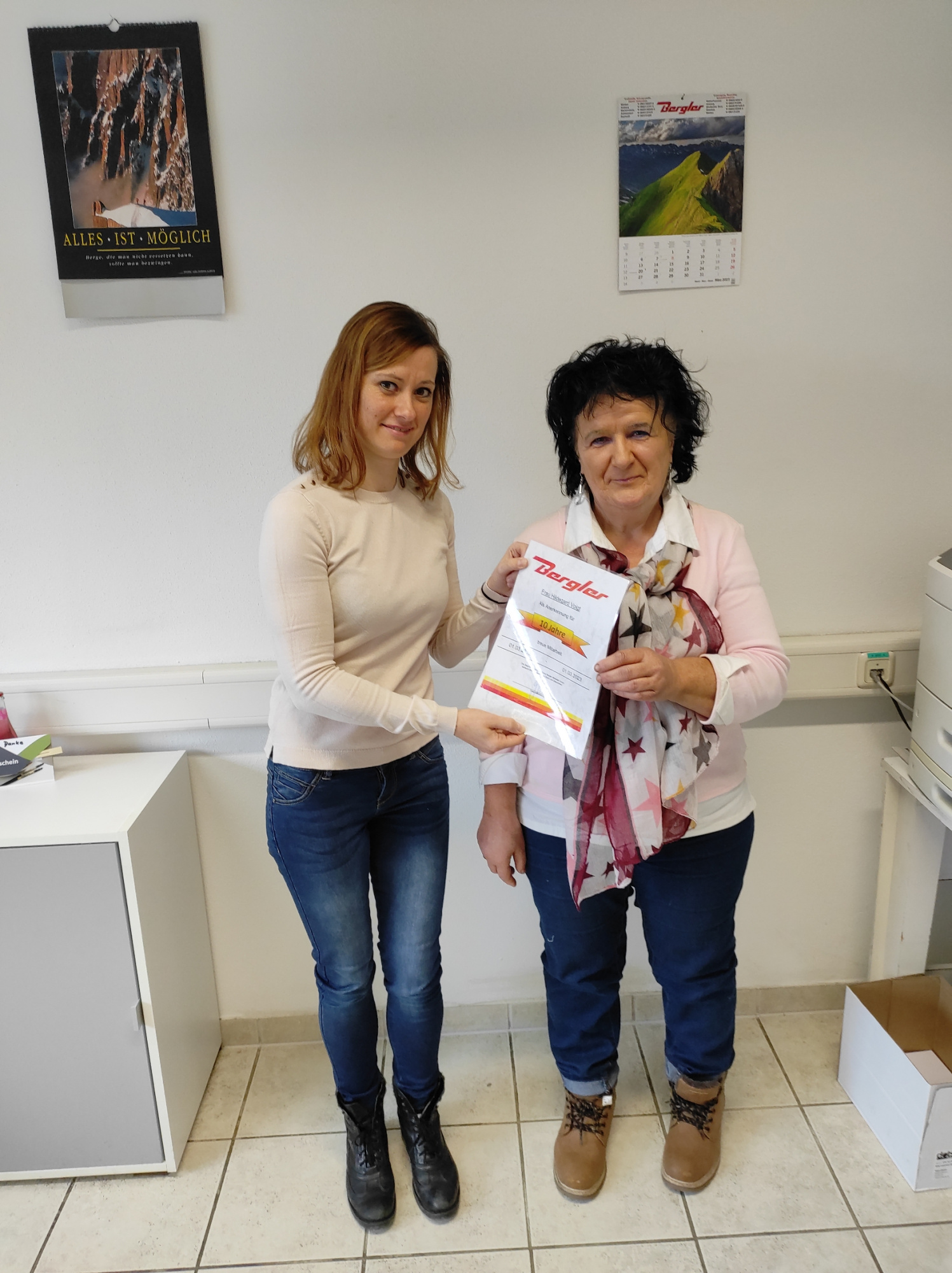 Zwei Damen stehen im Büro in Marktredwitz. Grund ist ein Betriebsjubiläum. Die linke Dame, eine Kollegin des Verkaufteams, überreicht der Jubilarin die Urkunde.