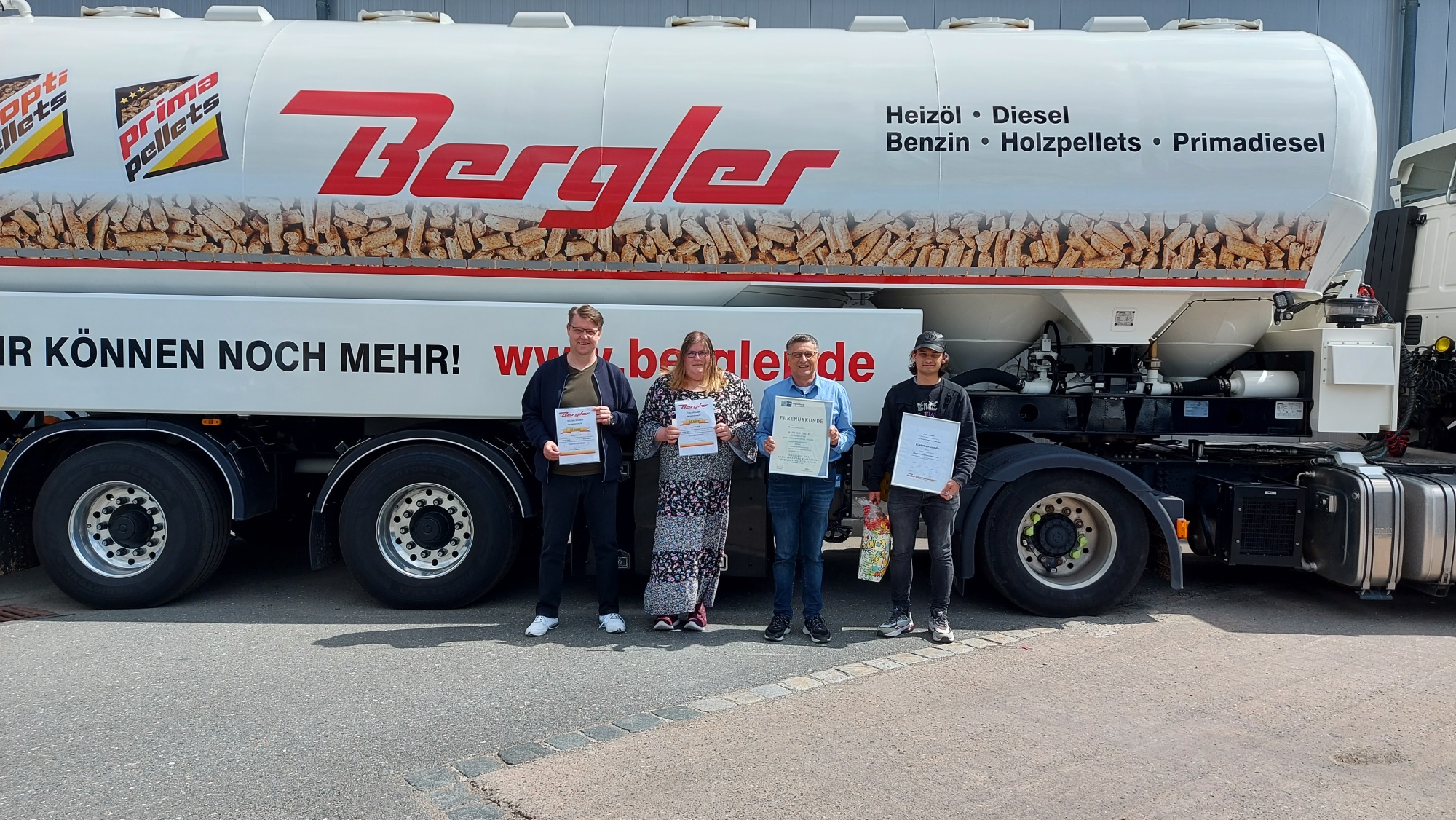Im Vordergrund die vier Jubilare der Bergler Mineralöl GmbH in Weiden, die ihre Urkunden in den Händen halten. Im Hintergrund ein parkender Pellets-LKW mit dem Bergler Logo sowie der Aufschrift Heizöl, Diesel, Benzin, Holzpellets, Primadiesel.