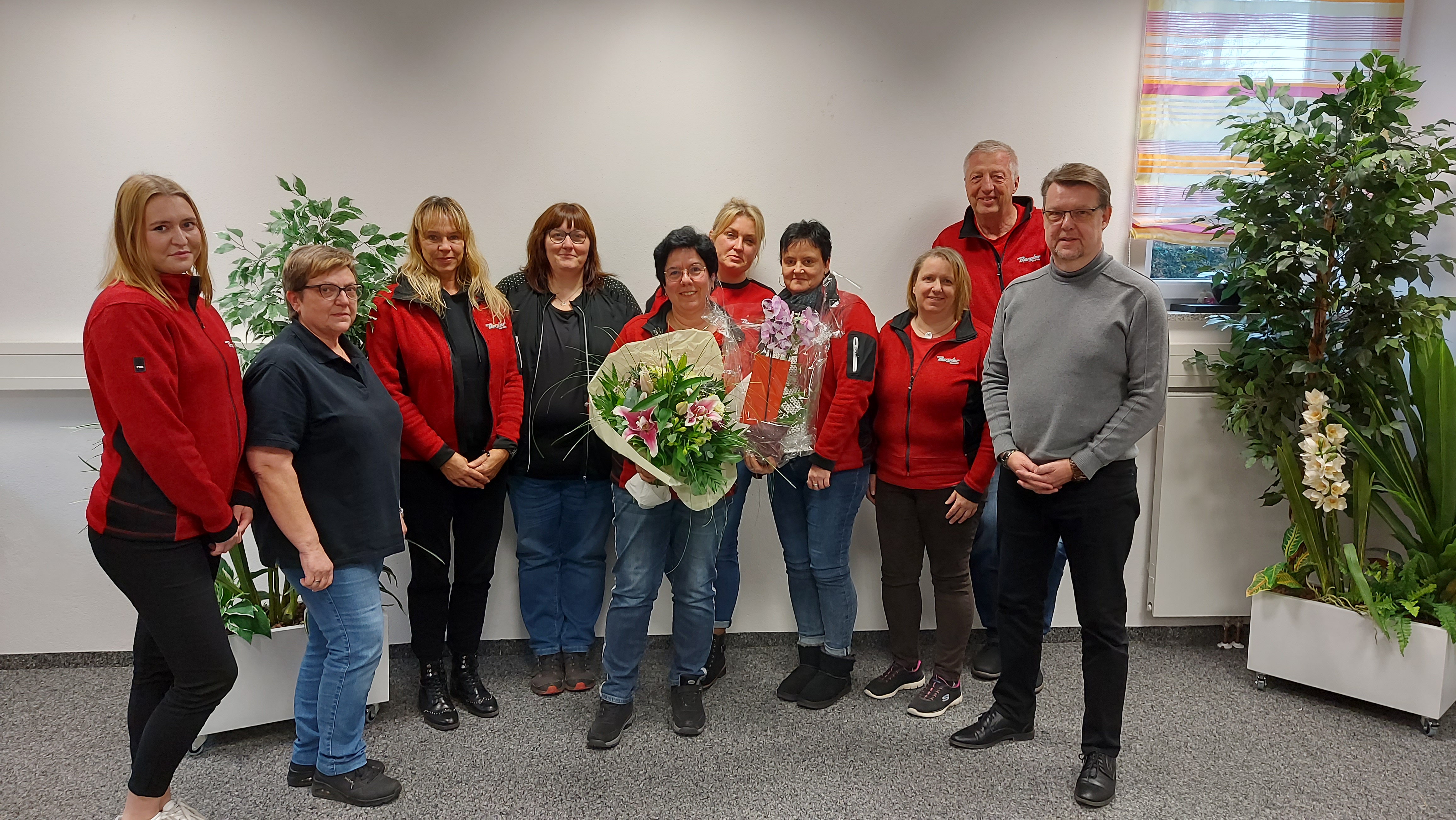 Michaela Winkler (mittig) hält Blumenstrauß und ein Geschenk in der Hand. Umringt wird sie von den Tankstellenleitungen.