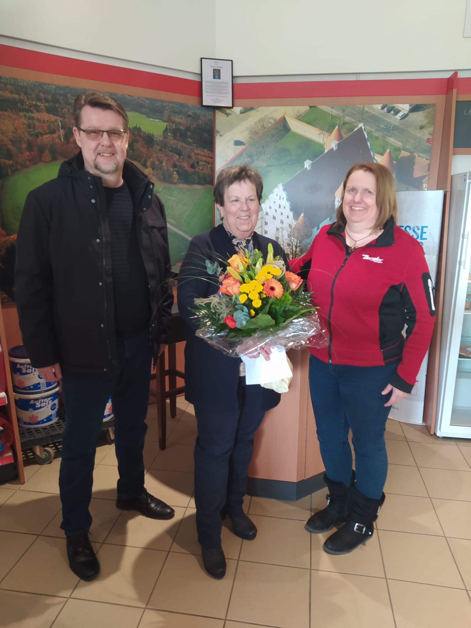 Peter Schneider, links, überreicht Christine Bock, mittig, einen großen bunten Blumenstrauß. Rechts Alexandra Mittlmeier, die Tankstellenleitung