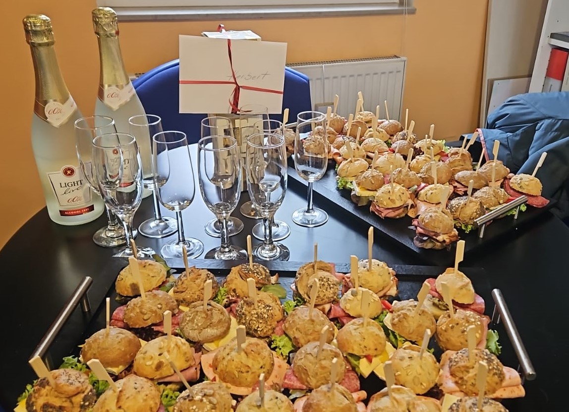 Kleine Verabschiedungsfeier mit Sekt und kleinen belegten Semmeln auf einem Tisch. Links der Sekt und rechts die Häppchen.