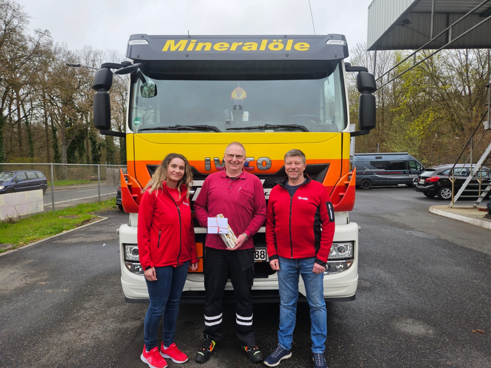Links Frau Lautenbach (Personal) überreicht feierlich zusammen mit Herr Stammler (Betriebsleiter Großhandel Amberg) (steht rechts im Bild) ein kleines Geschenk für Herrn Donhauser (Fahrer Großhandel Amberg) (in der Mitte).