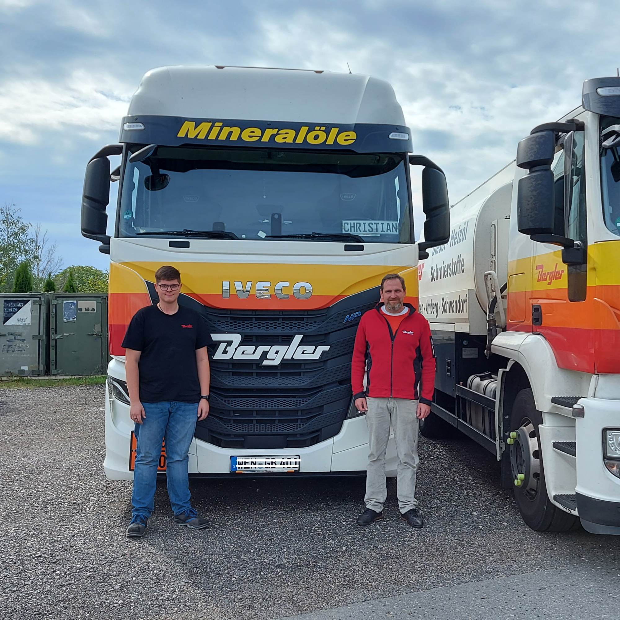 Im Vordergrund links steht Lukas Feddern, Auszubildender der Firma Bergler Mineralöl GmbH, mit schwarzem T-Shirt. Rechts daneben Geschäftsführer Gerhard Bergler mit roter Jacke. Beide stehen vor einem Tankwagen/ LKW. Über der Windschutzscheibe steht Mineralöle, unter der Scheibe sind die Bergler-Streifen in gelb, orange, rot abgebildet.
